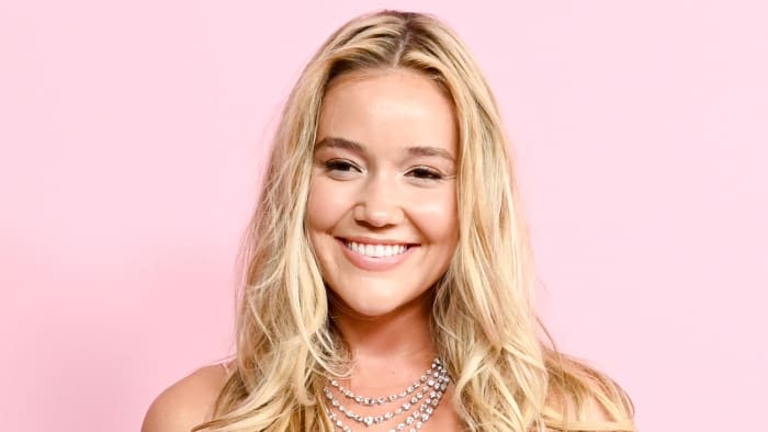 Olivia Ponton poses in a diamond necklace in front of a pink backdrop.